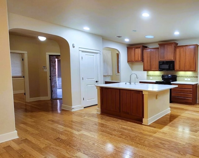 kitchen with black appliances, sink, decorative backsplash, light wood-type flooring, and an island with sink