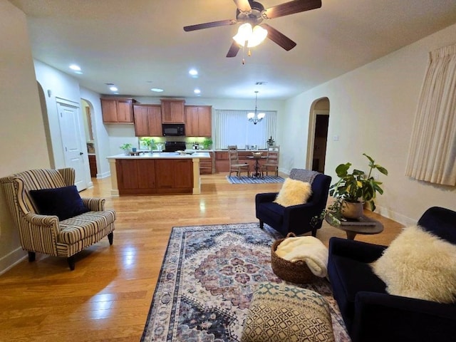 living room with light wood-type flooring, baseboards, arched walkways, and ceiling fan with notable chandelier