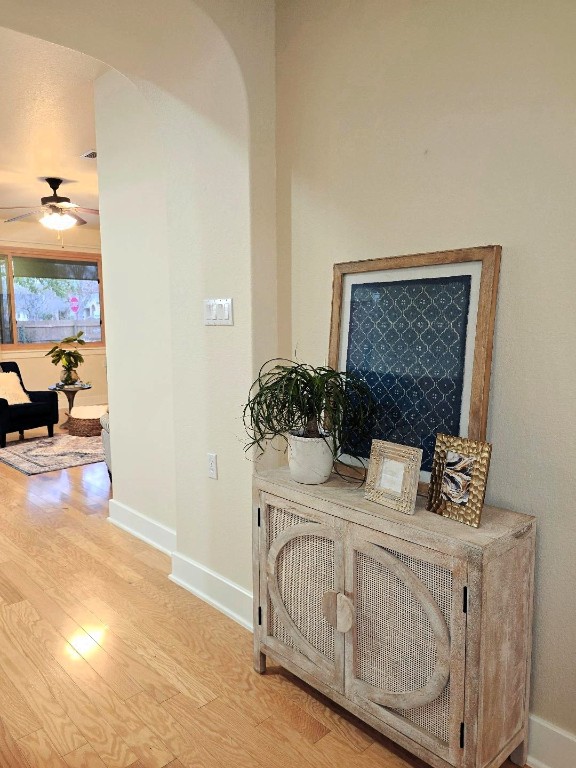 hall featuring light wood-type flooring, arched walkways, and baseboards