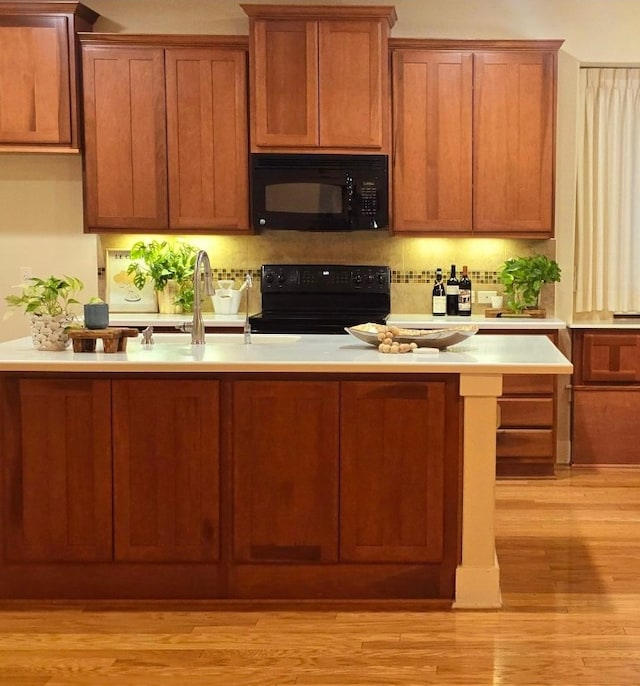 kitchen featuring black appliances, brown cabinetry, light wood-type flooring, and light countertops