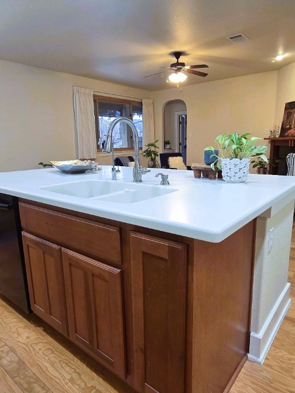 kitchen featuring arched walkways, light countertops, visible vents, brown cabinetry, and a sink