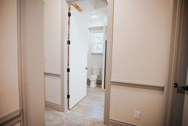 hall with light carpet and a textured wall