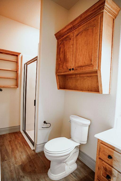 bathroom with wood finished floors, a shower stall, toilet, and baseboards