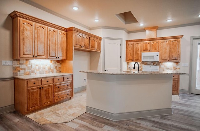 kitchen with white microwave, brown cabinetry, and a center island with sink