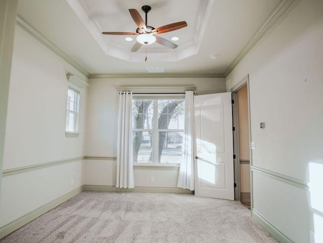 spare room with light carpet, a tray ceiling, baseboards, and crown molding