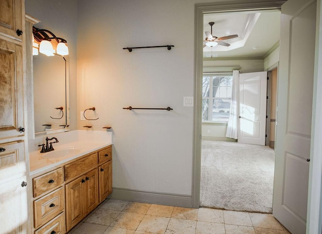 bathroom featuring a tray ceiling, ornamental molding, ceiling fan, vanity, and baseboards