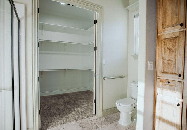 bathroom featuring a spacious closet, toilet, and baseboards