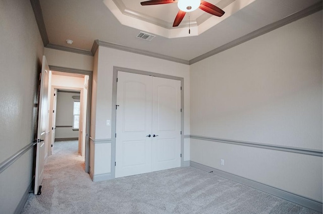 unfurnished bedroom with a raised ceiling, light colored carpet, a closet, visible vents, and ornamental molding