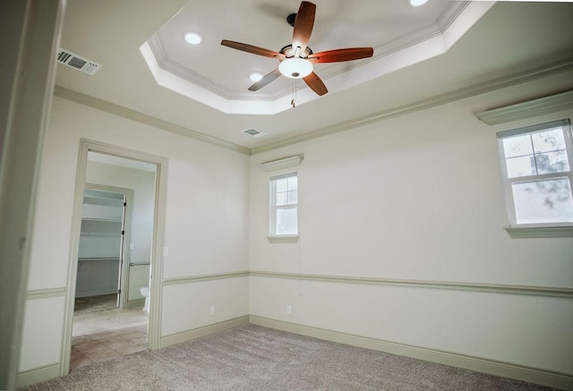 spare room with a tray ceiling, light colored carpet, crown molding, and visible vents