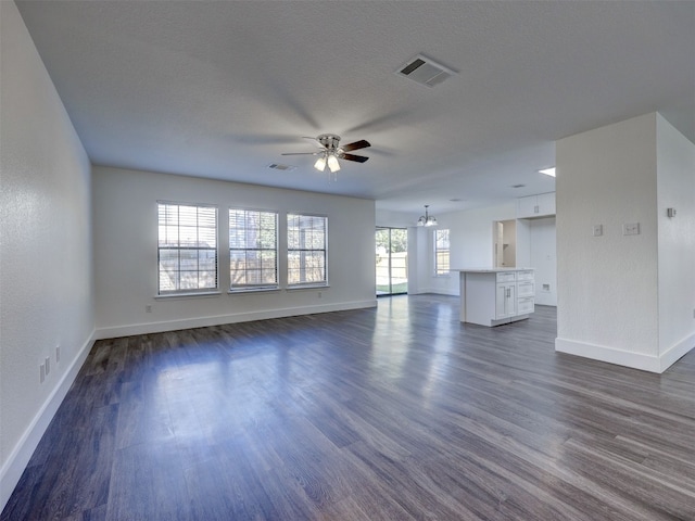 unfurnished living room with a textured ceiling, dark wood-type flooring, and ceiling fan with notable chandelier