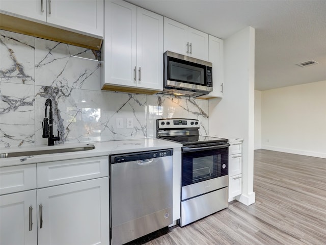 kitchen with white cabinets, sink, decorative backsplash, light hardwood / wood-style floors, and stainless steel appliances