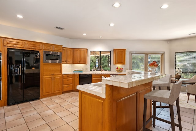 kitchen with tasteful backsplash, tile countertops, kitchen peninsula, light tile patterned flooring, and black appliances