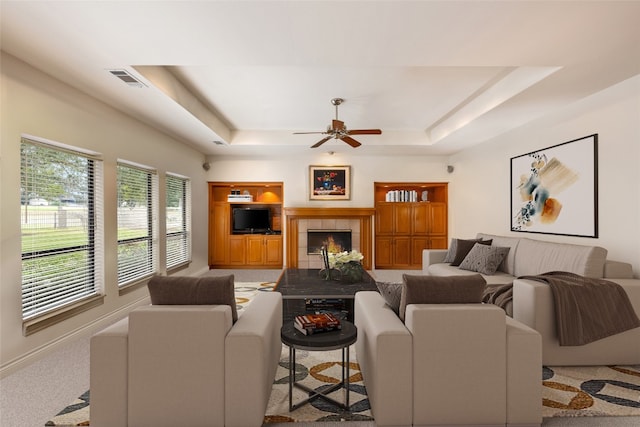 living room featuring carpet flooring, ceiling fan, a raised ceiling, and a tiled fireplace