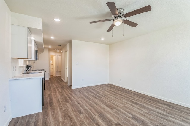 kitchen with ceiling fan, stainless steel stove, wood-type flooring, a textured ceiling, and white cabinets