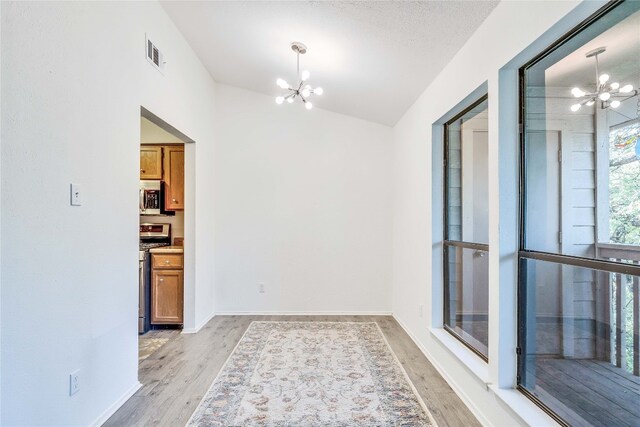 empty room with a textured ceiling, light hardwood / wood-style floors, an inviting chandelier, and lofted ceiling