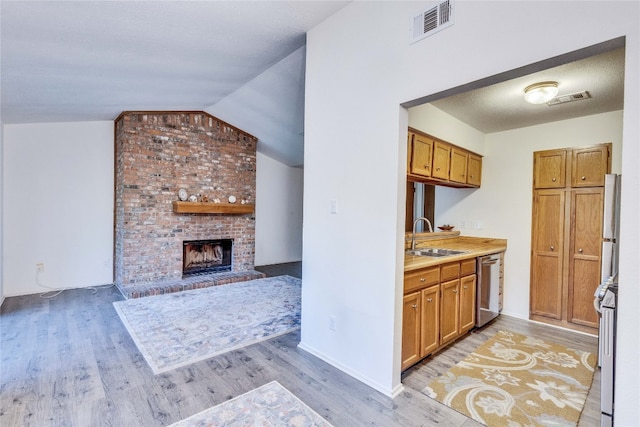 kitchen with a fireplace, light hardwood / wood-style floors, stainless steel dishwasher, and lofted ceiling