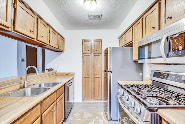 kitchen featuring sink, light hardwood / wood-style floors, a textured ceiling, and appliances with stainless steel finishes