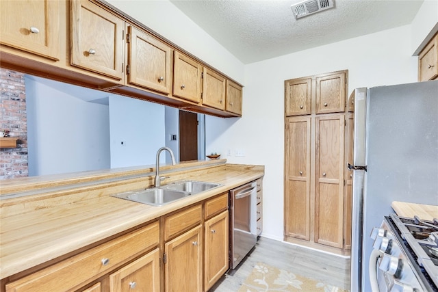 kitchen with a textured ceiling, stainless steel appliances, light hardwood / wood-style flooring, and sink