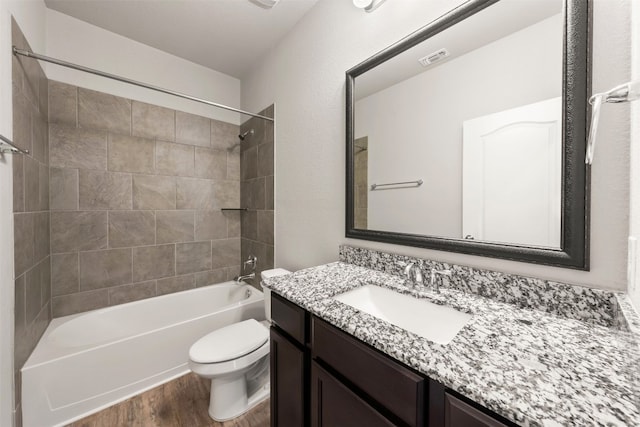 full bathroom featuring vanity, hardwood / wood-style floors, tiled shower / bath combo, and toilet