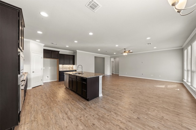 kitchen with sink, light stone counters, backsplash, a center island with sink, and hardwood / wood-style flooring