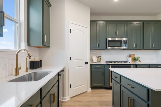 kitchen featuring sink, stainless steel appliances, green cabinets, backsplash, and light hardwood / wood-style floors