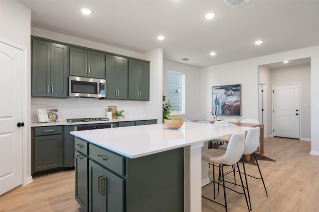 kitchen featuring tasteful backsplash, stainless steel appliances, light hardwood / wood-style flooring, a kitchen island, and green cabinets