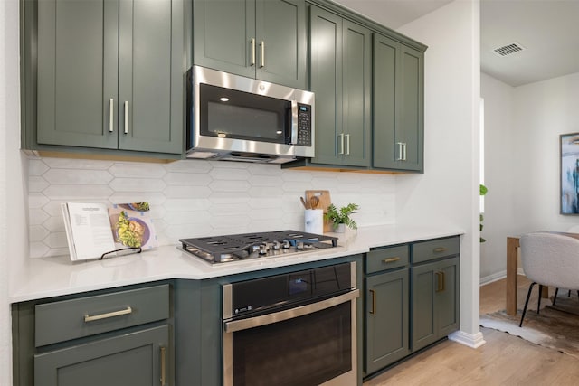 kitchen featuring tasteful backsplash, green cabinets, light hardwood / wood-style flooring, and appliances with stainless steel finishes