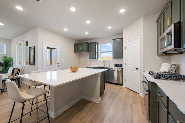 kitchen featuring tasteful backsplash, stainless steel appliances, sink, light hardwood / wood-style flooring, and a kitchen island