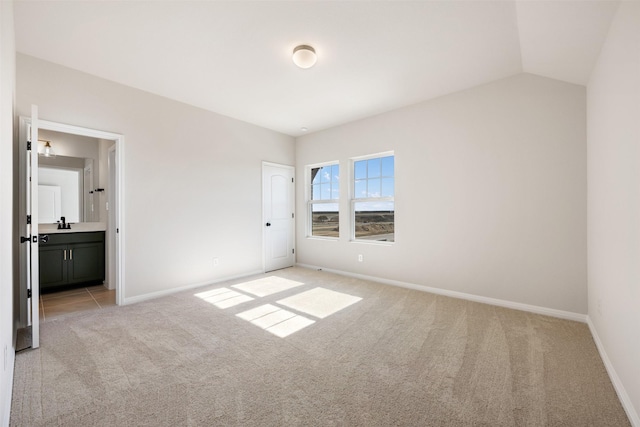 unfurnished bedroom featuring light carpet, ensuite bathroom, and lofted ceiling