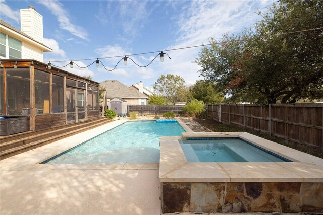 view of swimming pool with an in ground hot tub, a storage unit, and a sunroom