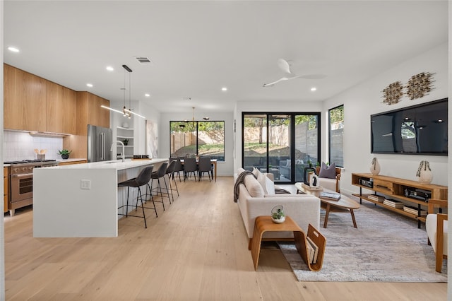 living room with light hardwood / wood-style flooring, ceiling fan with notable chandelier, and sink