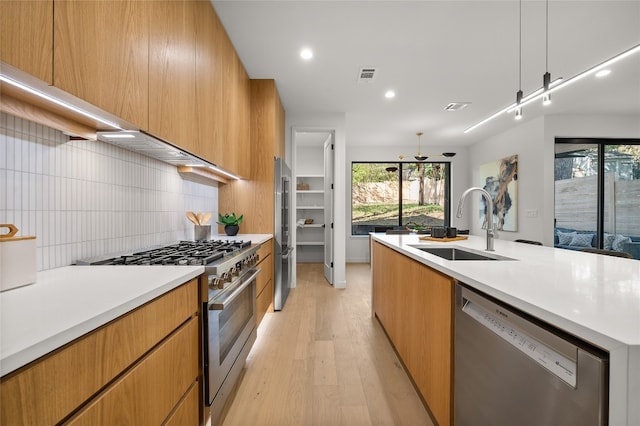 kitchen featuring appliances with stainless steel finishes, light wood-type flooring, tasteful backsplash, sink, and hanging light fixtures