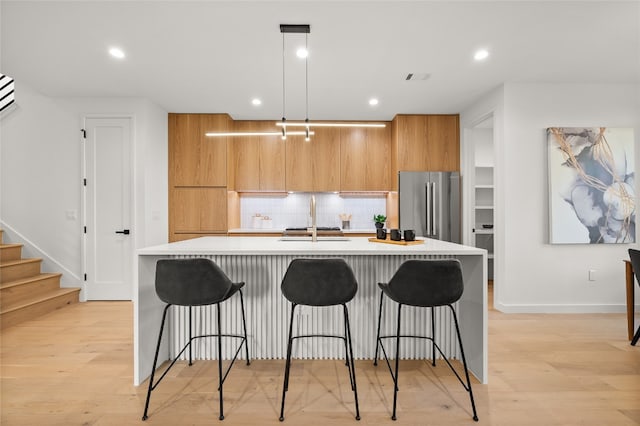 kitchen featuring high end refrigerator, a center island with sink, a kitchen breakfast bar, light wood-type flooring, and decorative light fixtures