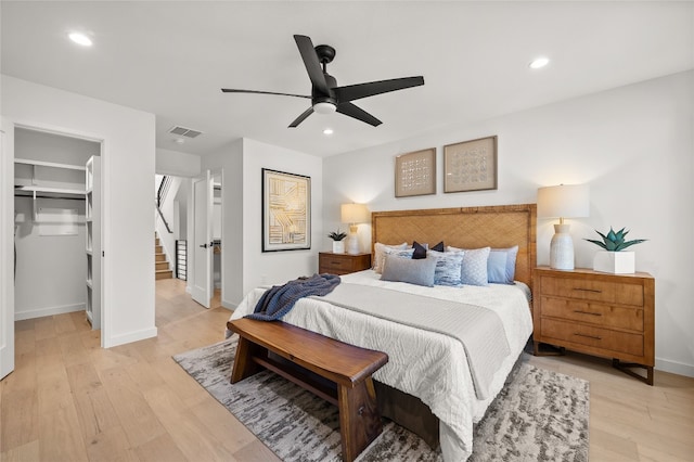 bedroom featuring a walk in closet, a closet, light hardwood / wood-style flooring, and ceiling fan