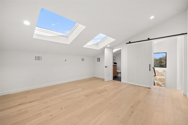 additional living space featuring light hardwood / wood-style floors, a barn door, and vaulted ceiling