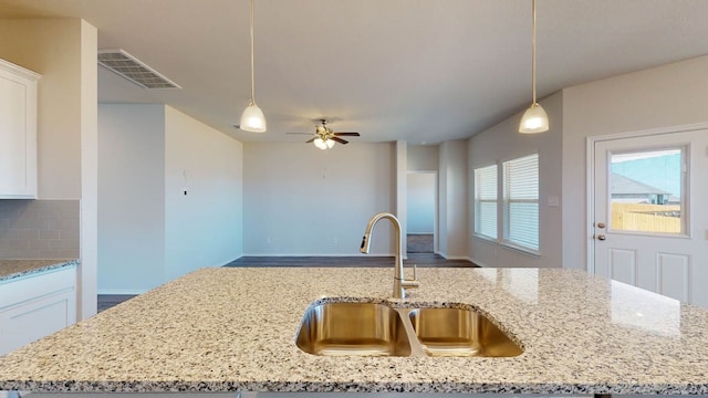 kitchen featuring white cabinets, light stone counters, hanging light fixtures, and sink