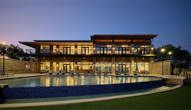 back house at dusk featuring a balcony and a patio area