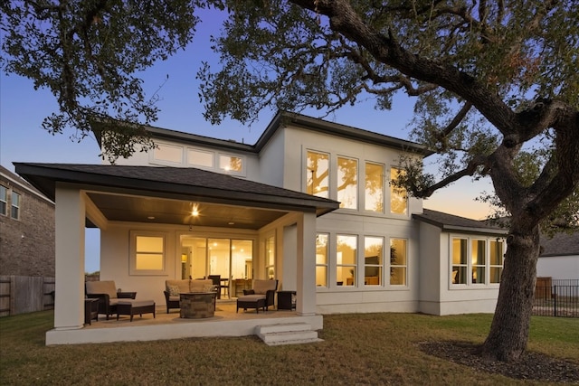 back house at dusk with an outdoor living space, a patio, and a lawn