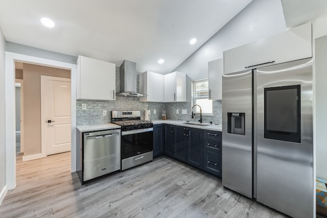 kitchen with appliances with stainless steel finishes, sink, wall chimney range hood, light hardwood / wood-style floors, and white cabinetry