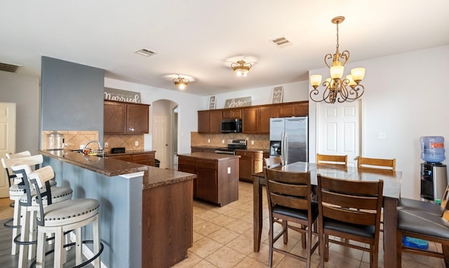 kitchen featuring a center island, an inviting chandelier, tasteful backsplash, kitchen peninsula, and stainless steel appliances