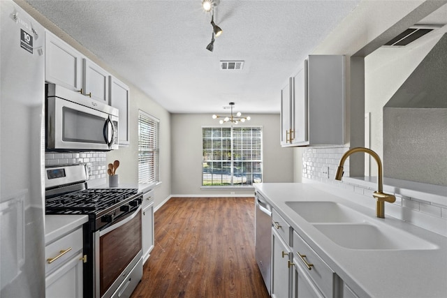 kitchen with appliances with stainless steel finishes, backsplash, dark wood-type flooring, sink, and a notable chandelier