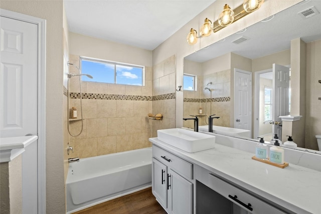 full bathroom with wood-type flooring, vanity, tiled shower / bath, and a healthy amount of sunlight