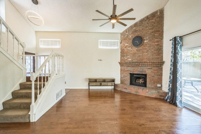 living room featuring wood-type flooring, vaulted ceiling, ceiling fan, and a brick fireplace