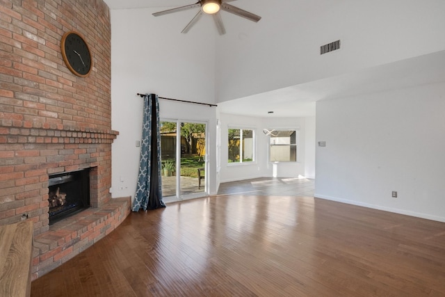 unfurnished living room with hardwood / wood-style flooring, ceiling fan, a fireplace, and a high ceiling