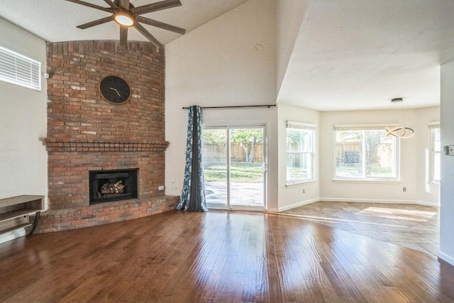 unfurnished living room with ceiling fan with notable chandelier, hardwood / wood-style flooring, a brick fireplace, and lofted ceiling