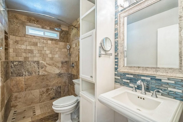 bathroom with backsplash, sink, tiled shower, and toilet