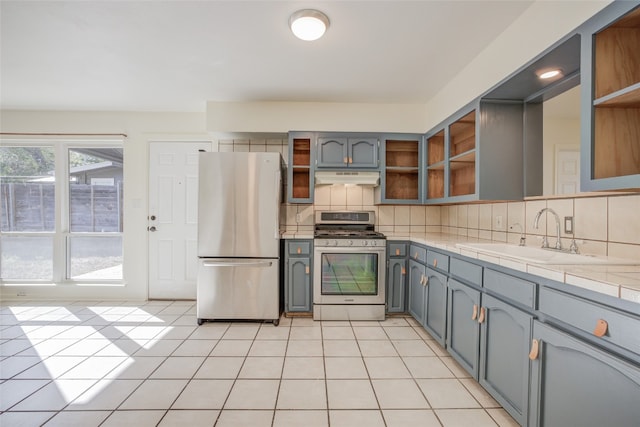 kitchen featuring appliances with stainless steel finishes, tasteful backsplash, sink, light tile patterned floors, and tile counters