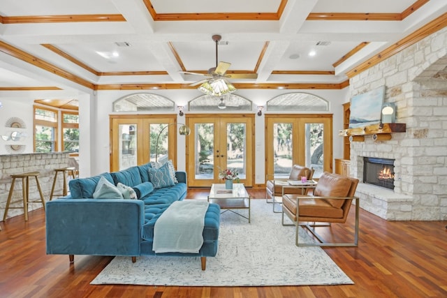 living room with ceiling fan, french doors, dark wood-type flooring, a stone fireplace, and beamed ceiling