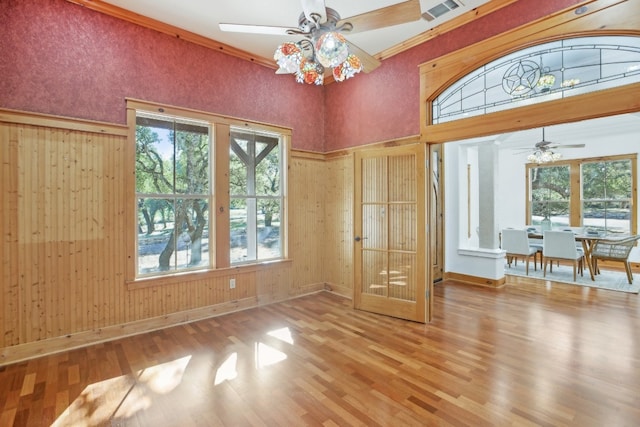 interior space with ceiling fan, french doors, wood walls, hardwood / wood-style flooring, and ornamental molding