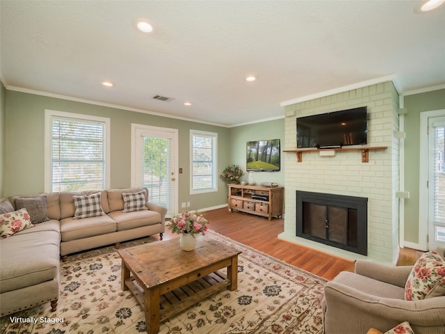 living room featuring hardwood / wood-style flooring, a healthy amount of sunlight, ornamental molding, and a brick fireplace